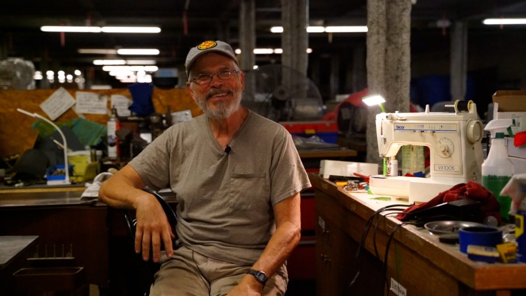 Joe Young sitting at his desk next to his current sewing machine repair project.