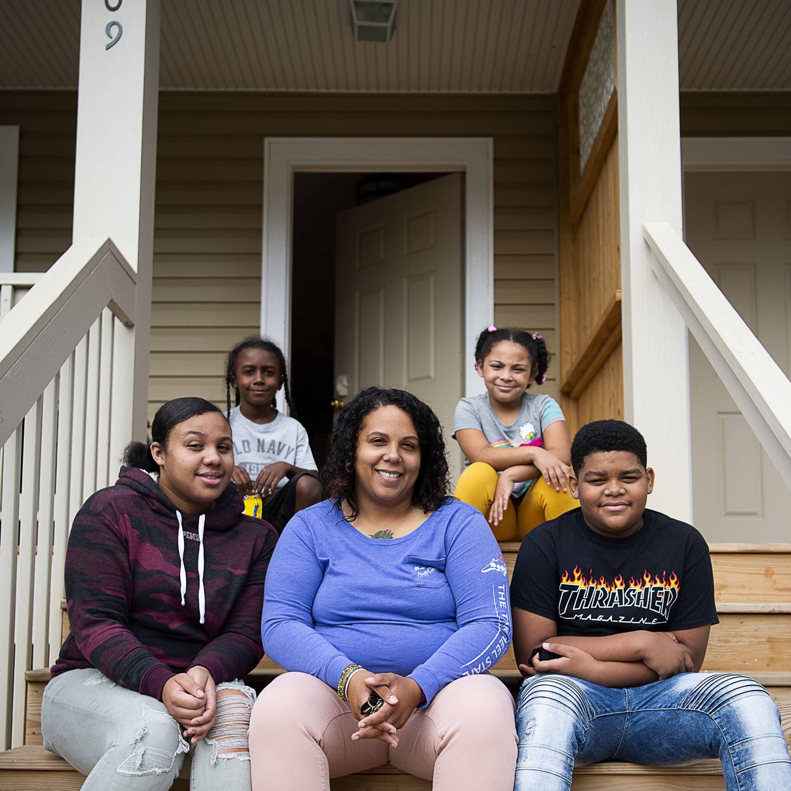 A young woman sits on the porch steps of her home surrounded by her four children