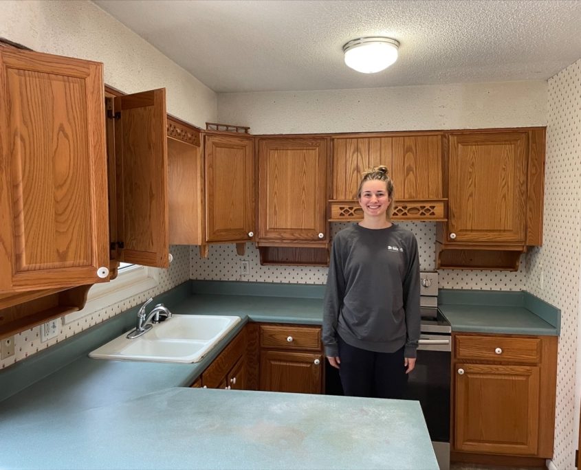Natalie stands in a kitchen prior to deconstructing the cabinets and countertops.
