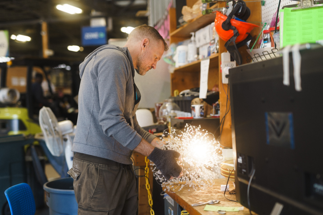 Bryan stands over an illuminated lighting fixture plugged into a power strip on a workbench.