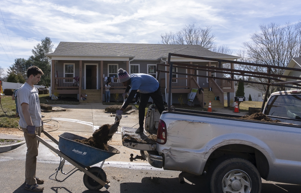 Two volunteers work together to shovel mulch from the back of a pickup truck into a wheelbarrow.