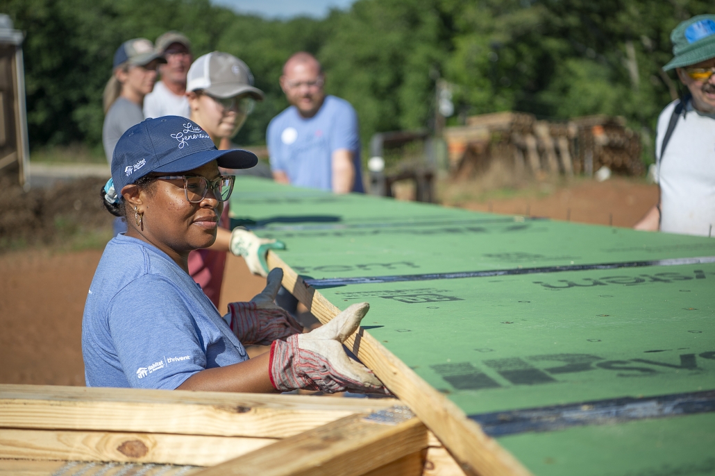 A volunteer group carries a wall panel on a Habitat jobsite